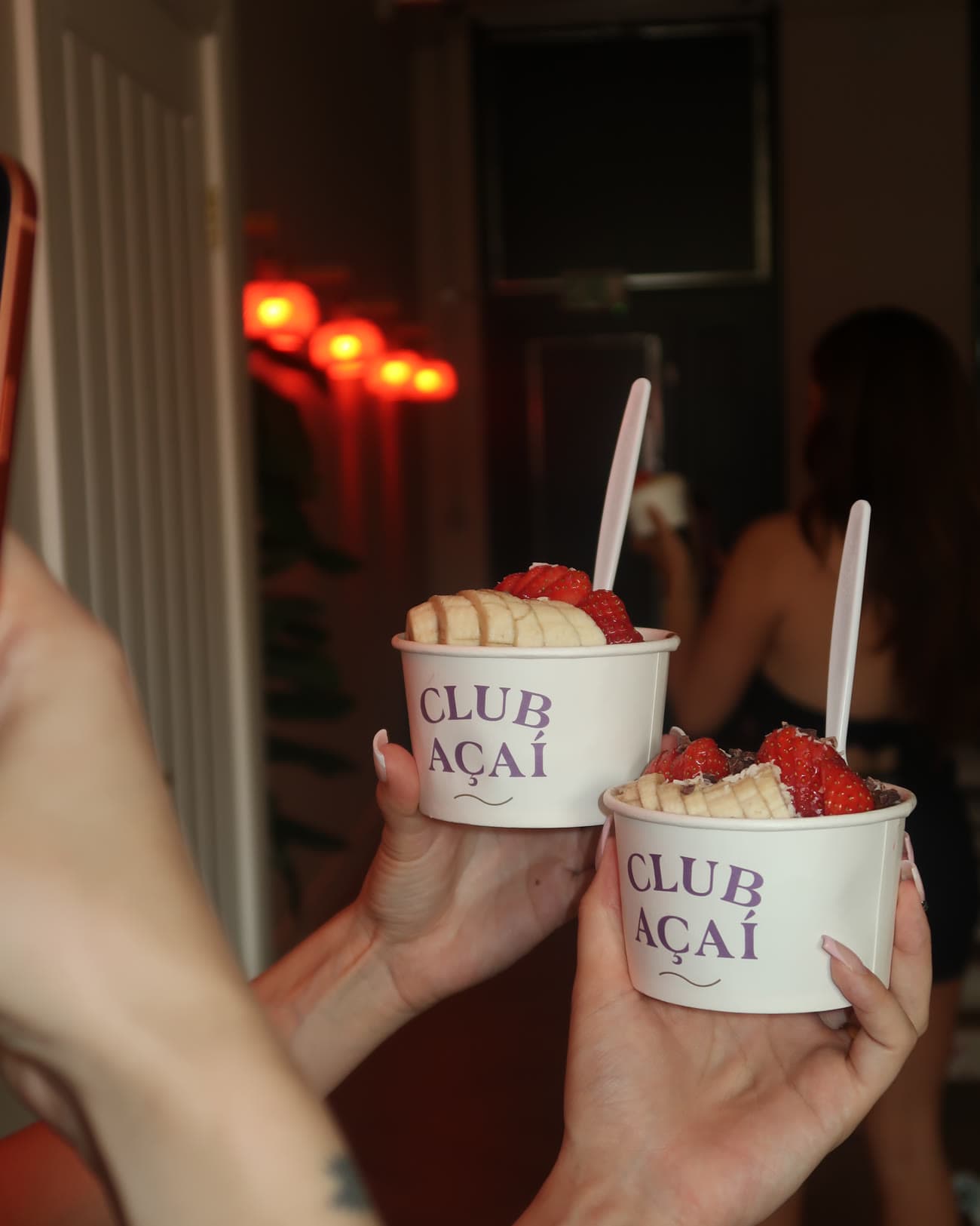 Two Club Açaí bowls held up in the neon lit studio