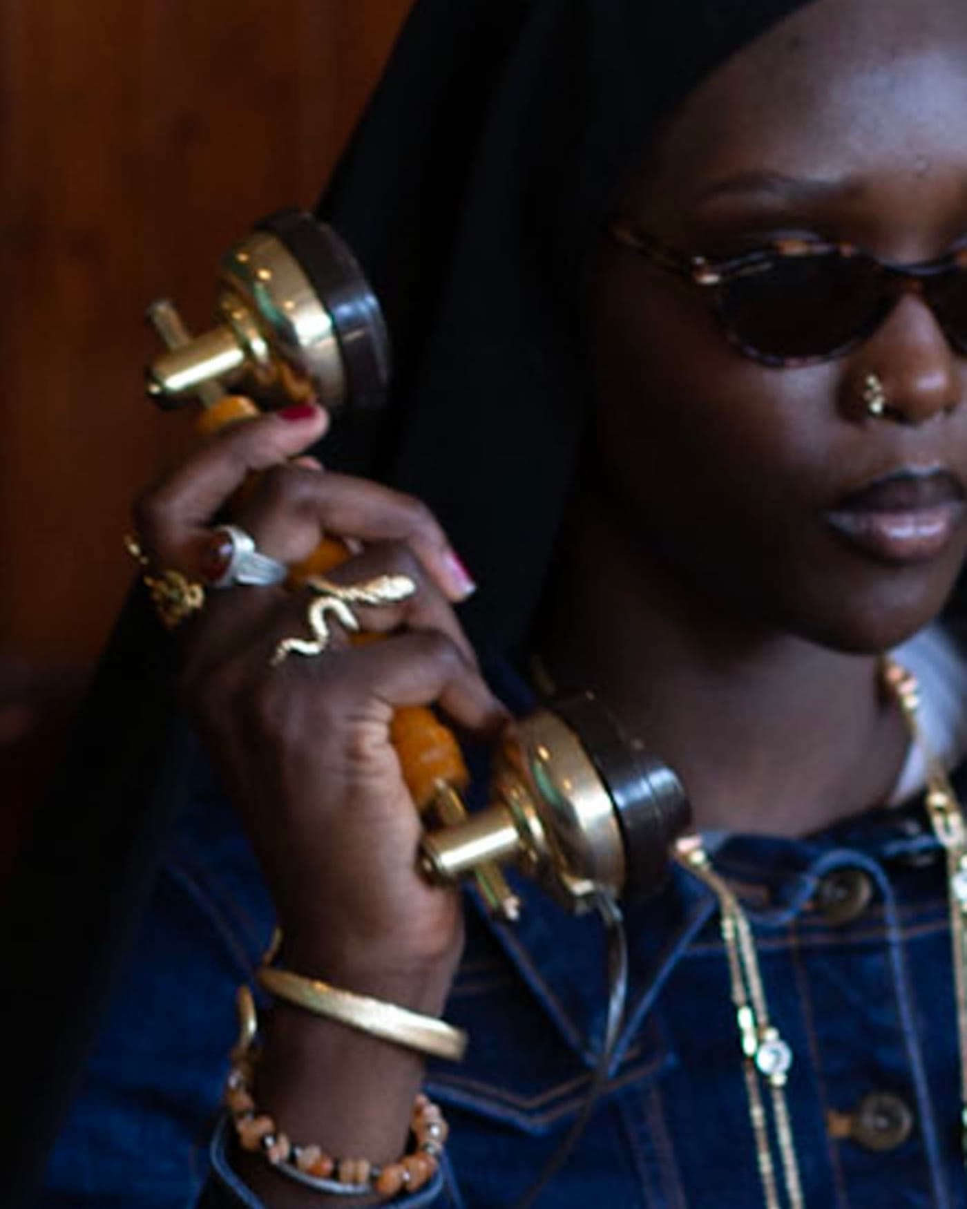 Detail frame, brass telephone held against denim and layered jewellery